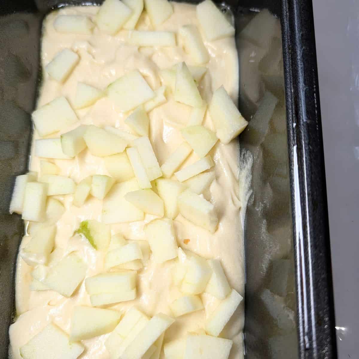 Layers of batter and diced apples in a loaf pan.