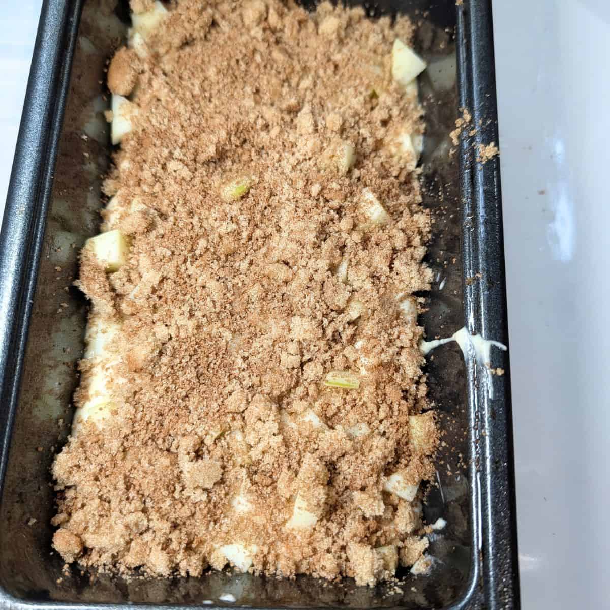 Apple cinnamon bread batter layered with chopped apples and cinnamon sugar in a loaf pan.