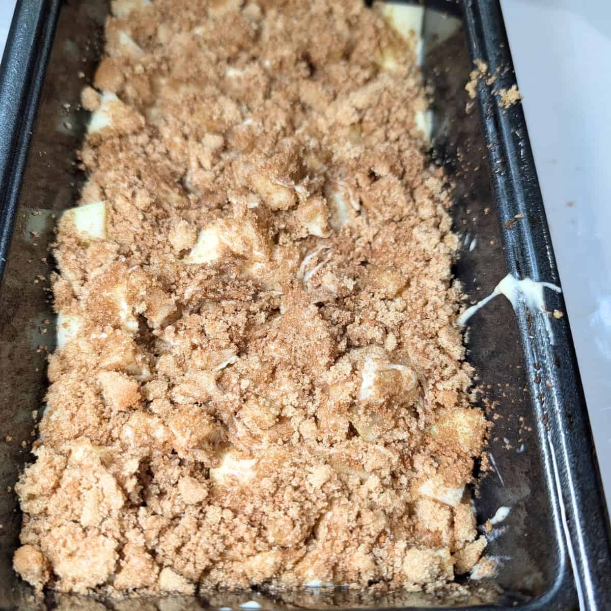 Apple cinnamon bread batter layered with chopped apples and cinnamon sugar in a loaf pan.
