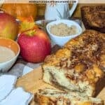 Picture of apple cinnamon bread on a wooden table decorated with apples, cinnamon, and brown sugar.