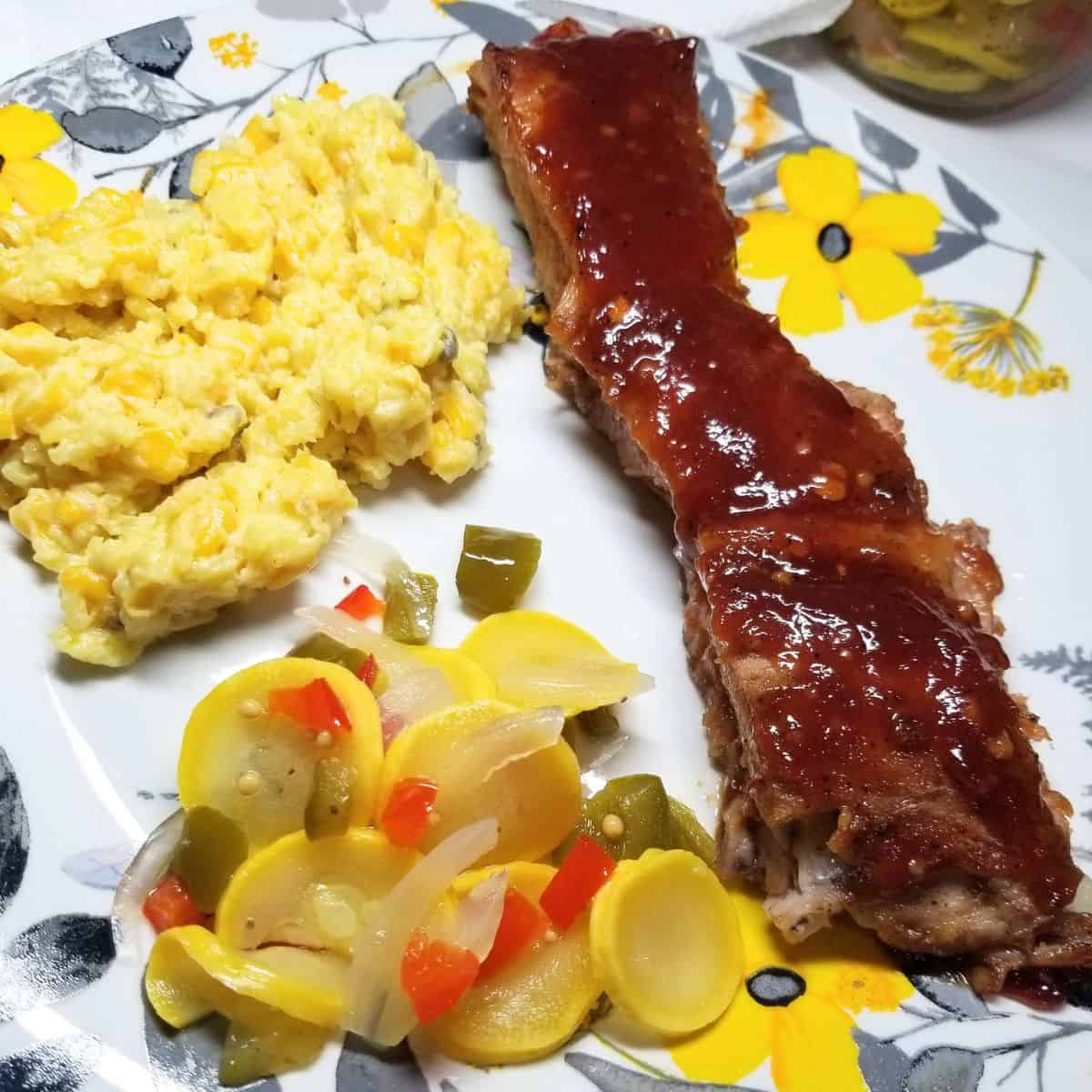 Tender fall-off-the-bone BBQ ribs fresh from the oven with caramelized barbecue sauce on a plate with a few sides.