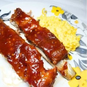 Baked barbecue ribs on a plate with a side of rice.