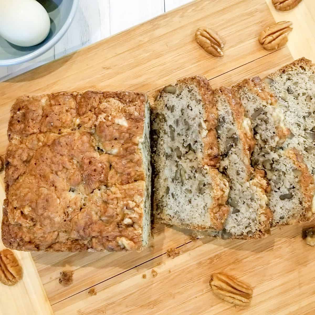 Sliced banana nut bread with pecans on wooden cutting board.
