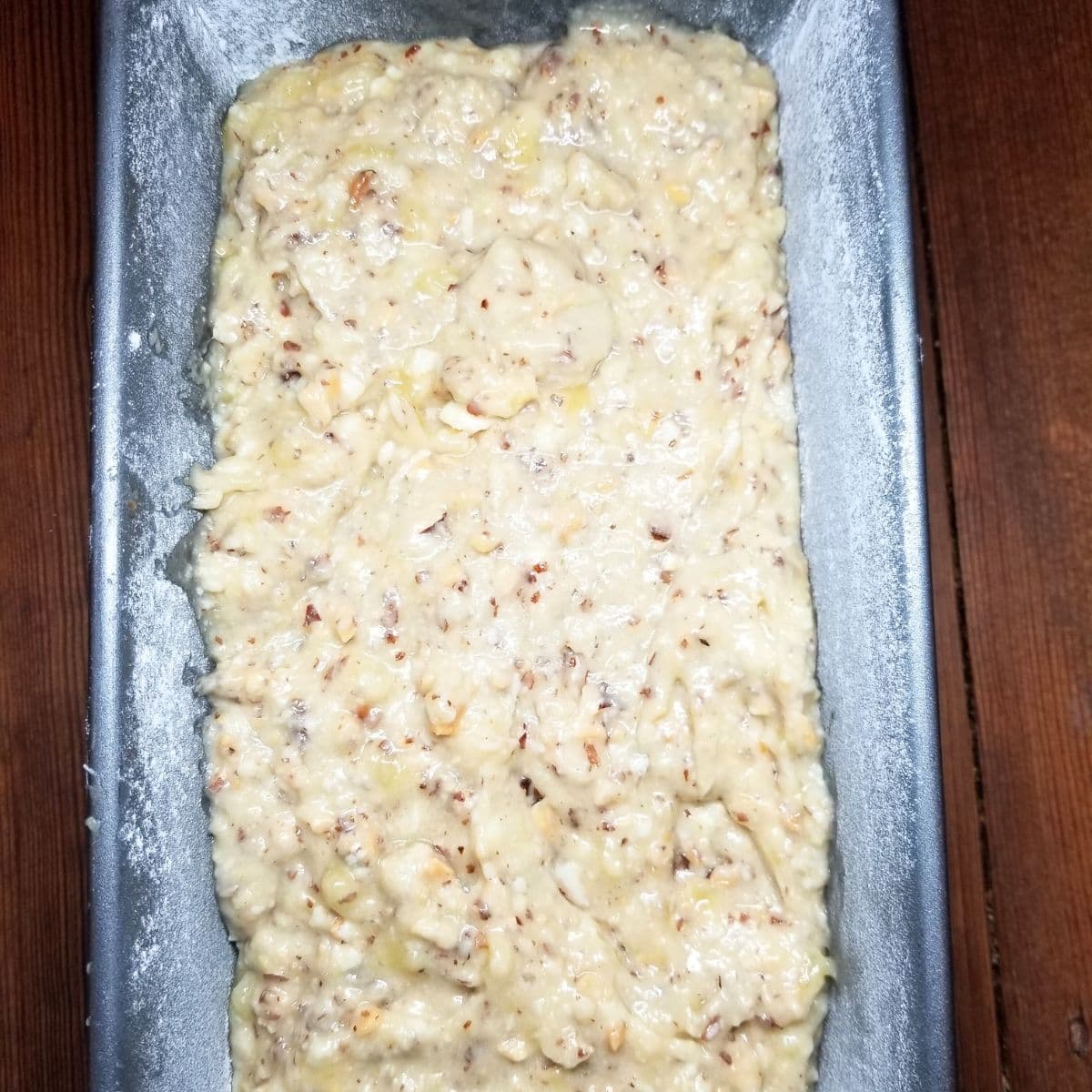 Pouring banana nut bread batter into greased loaf pan.