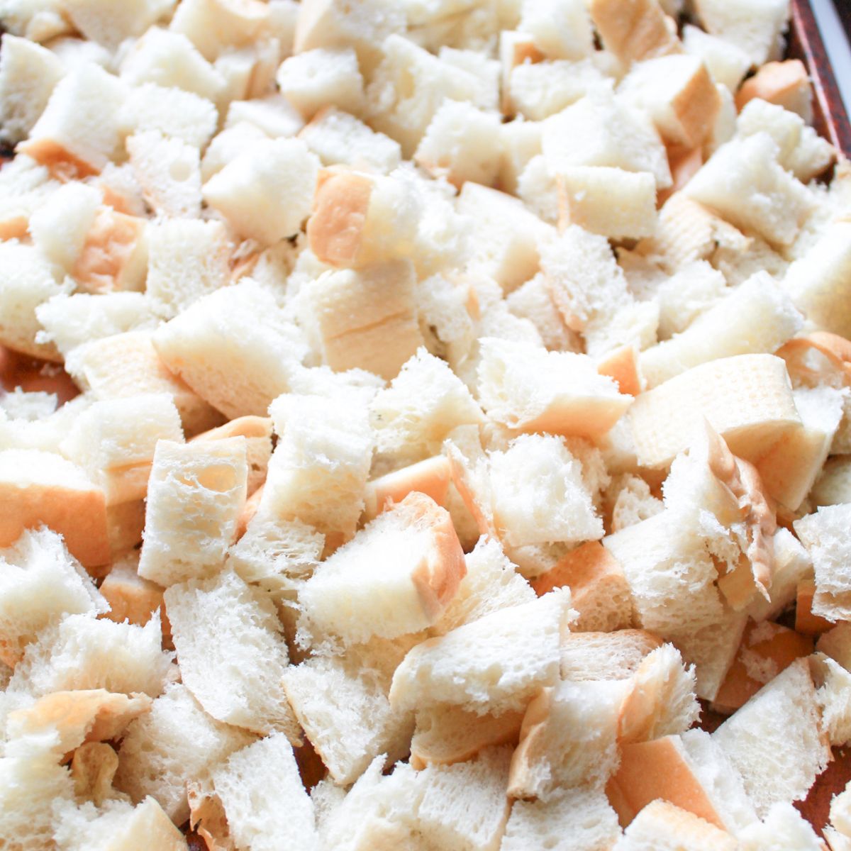 Cubed brioche bread drying on a baking sheet in the oven.