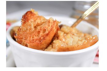 Bread pudding with whiskey sauce shown in a white bowl with a spoon.