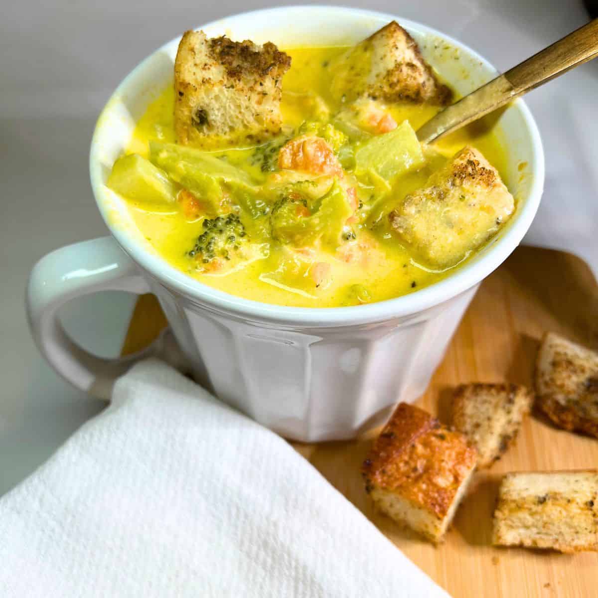 Cooked soup in white bowl with a gold spoon. Croutons and a white napkin next to the bowl.