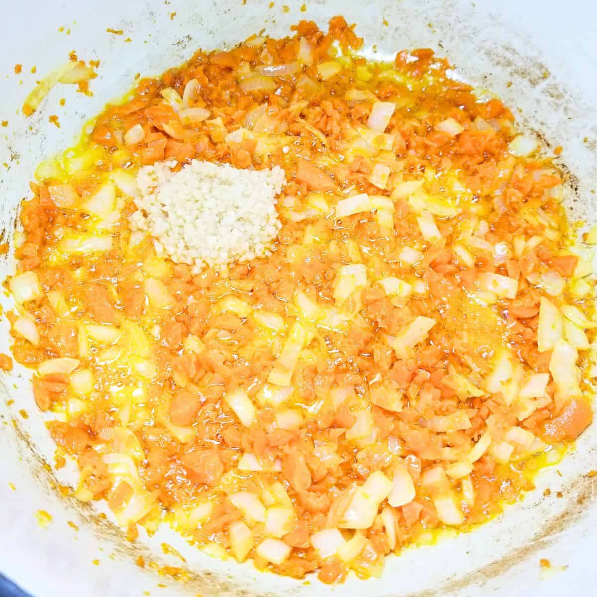 Minced garlic added to carrots and onion in a soup pot.