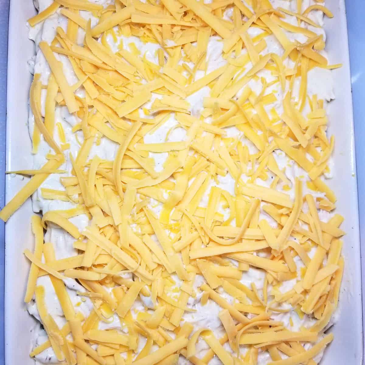 Shredded cheddar cheese sprinkled over chicken casserole before cracker topping.