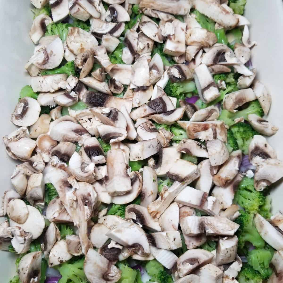 Diced onion, broccoli, and mushrooms layered over crescent dough in casserole dish.