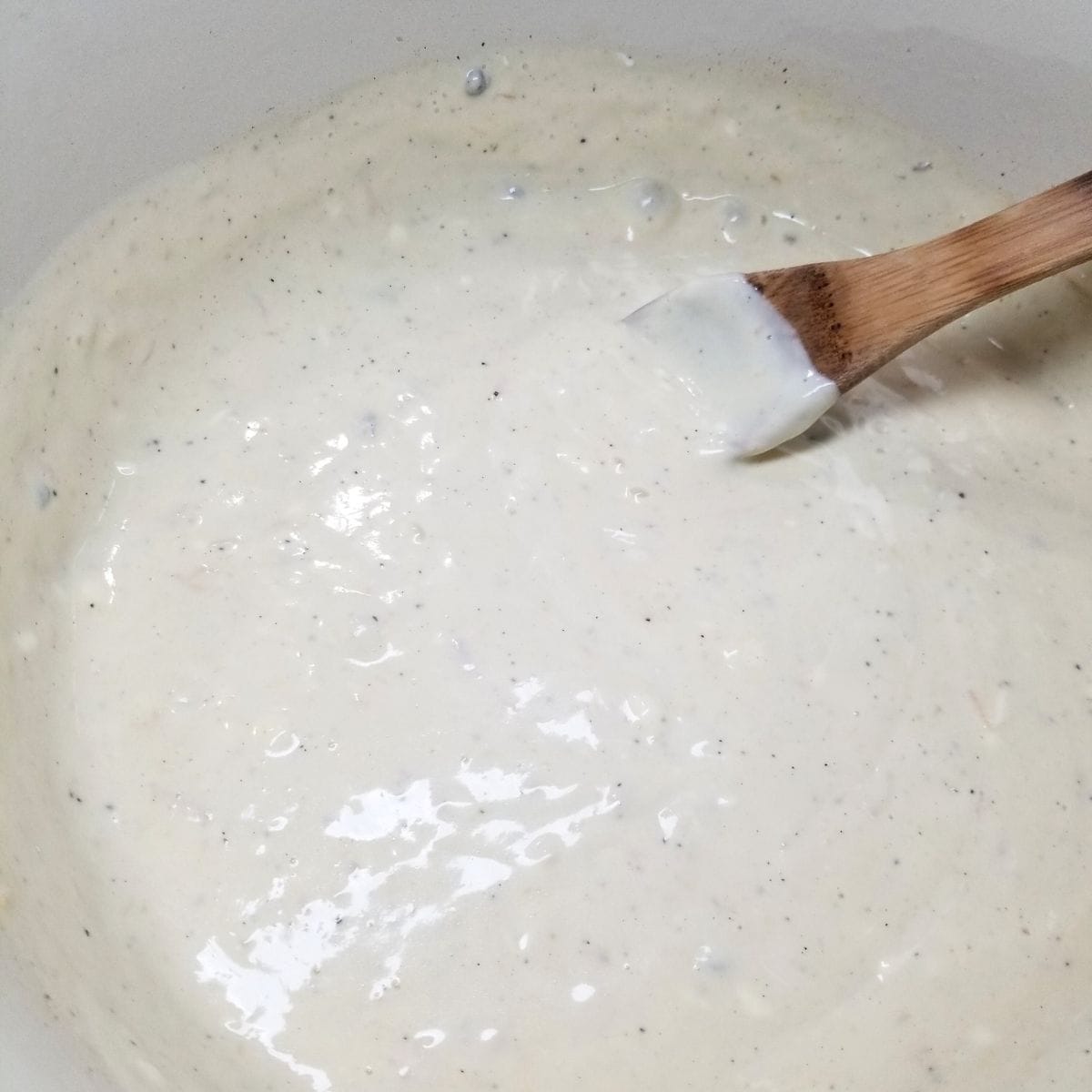 Creamy sauce with cream cheese melting in saucepan on stovetop.