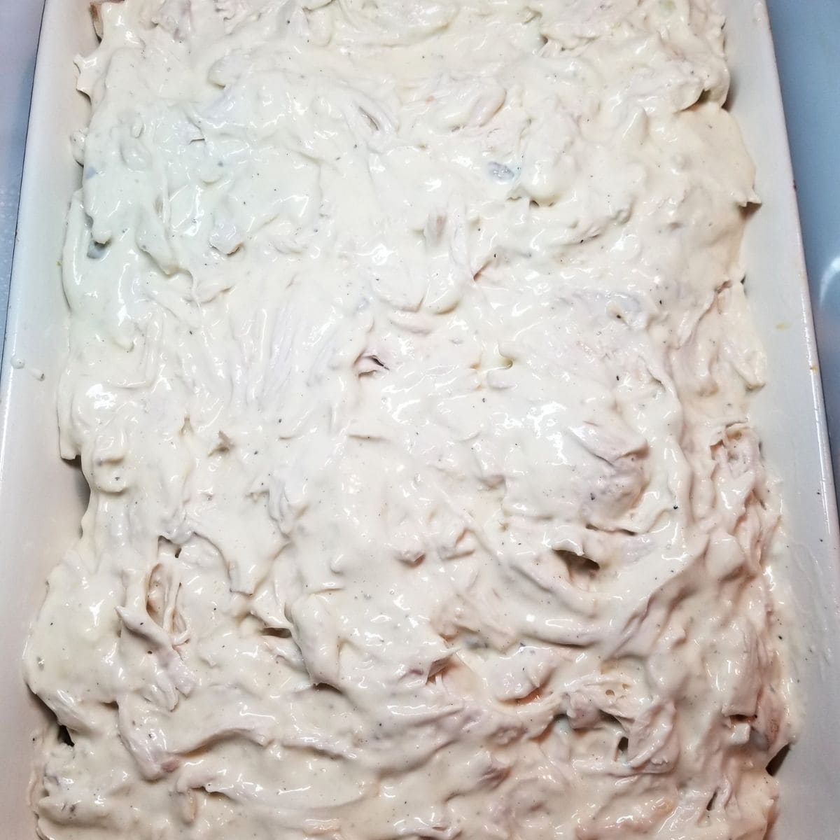 Chicken mixture poured over vegetables in baking dish before adding cheese.