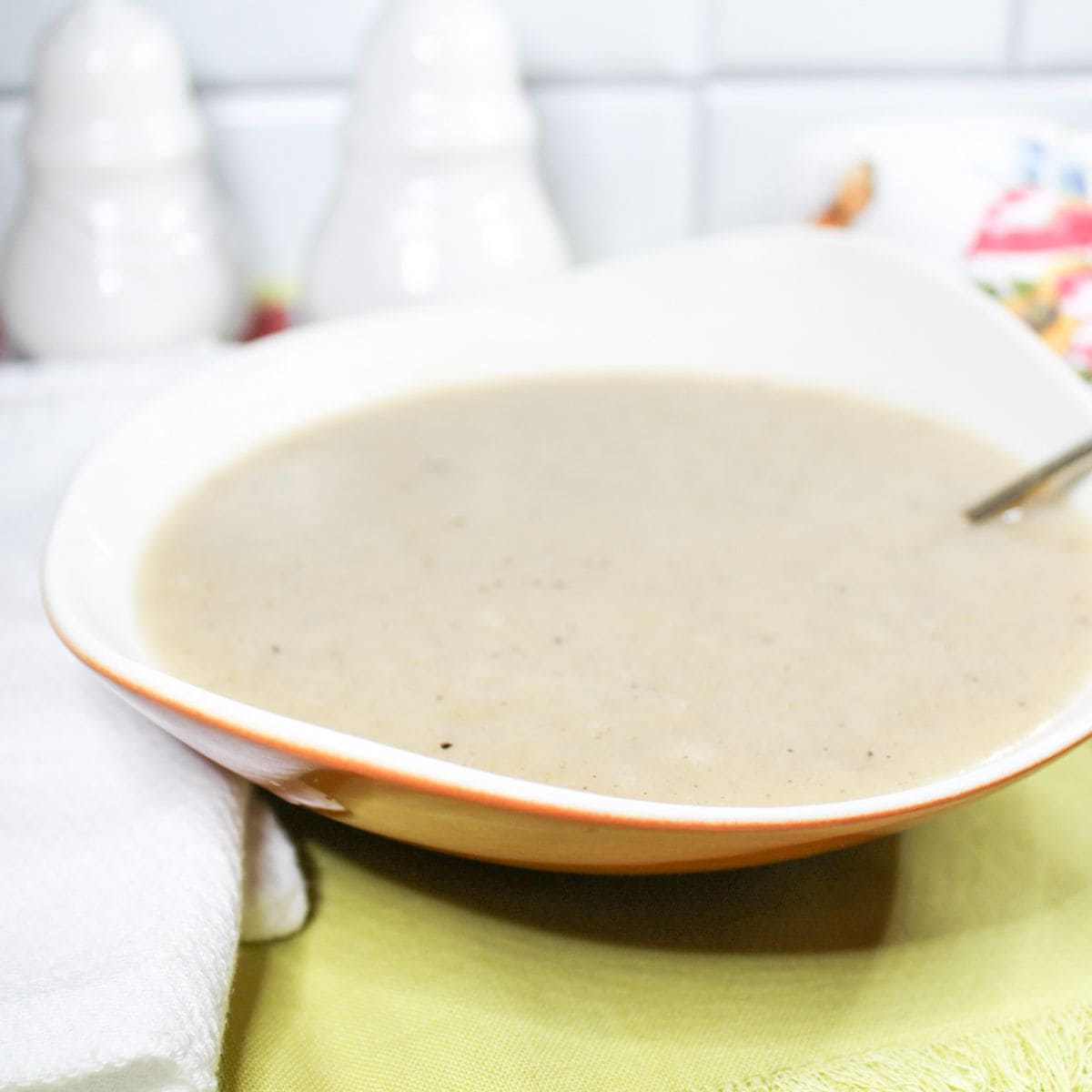 Brown gravy in a white bowl with a spoon. Green and white dish towels. 