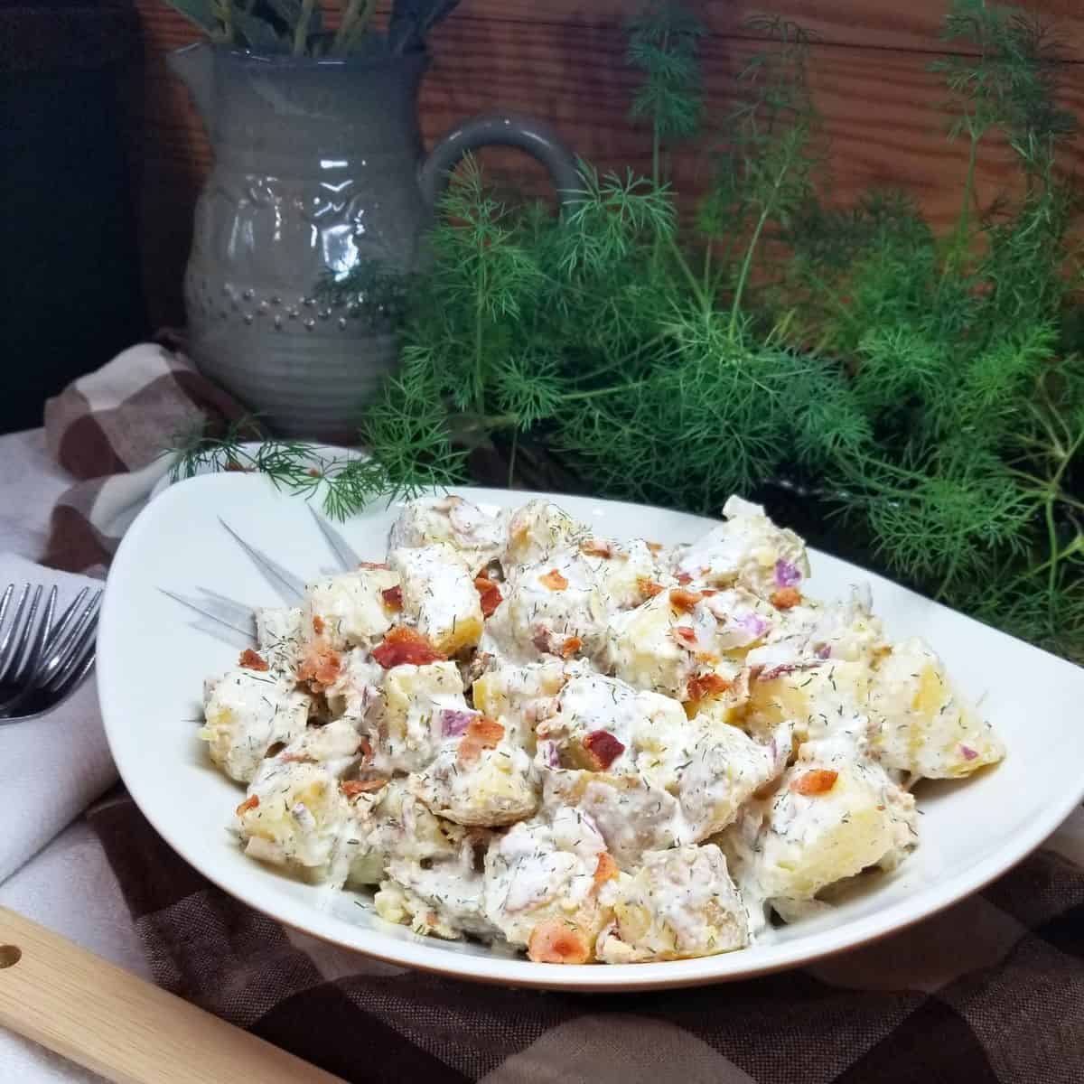 Cold potato salad in a bowl sitting on a farmhouse table.