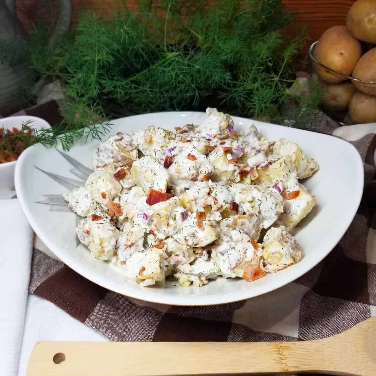 Cold potato salad in a bowl sitting on a farmhouse table.