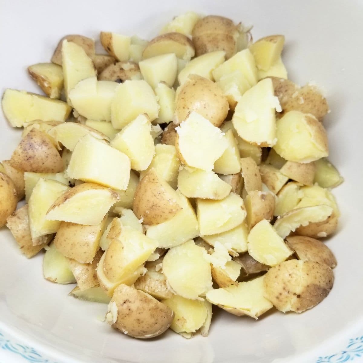 Cutting cooked potatoes into bite-sized pieces on cutting board and adding them to a bowl.