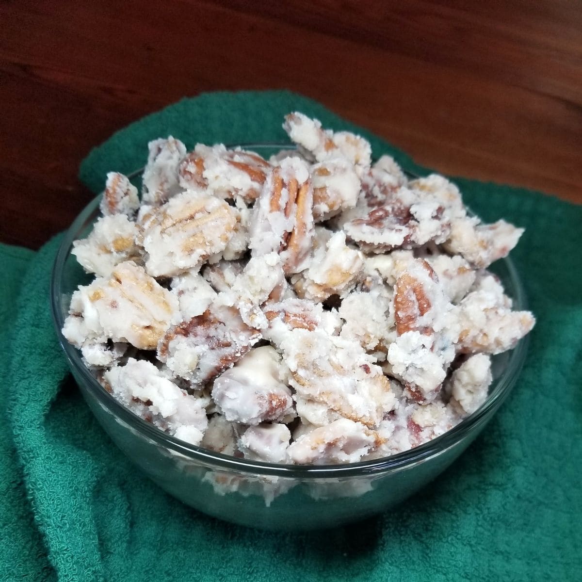 Candied pecans in a bowl with a green dish towel under the bowl.