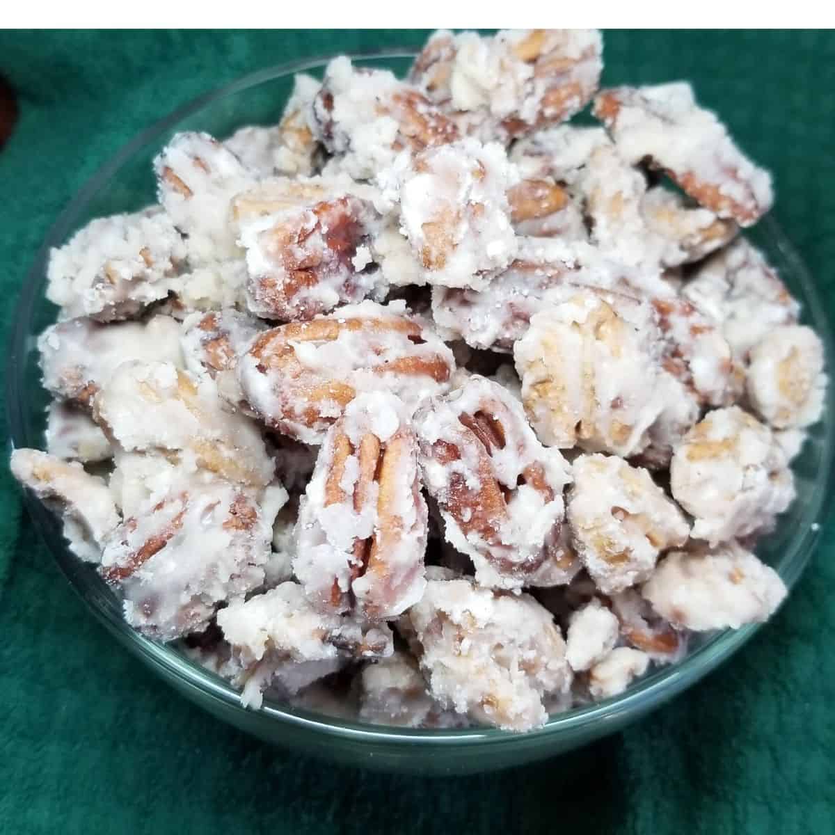 Candied pecans in a bowl with a green dish towel under the bowl.