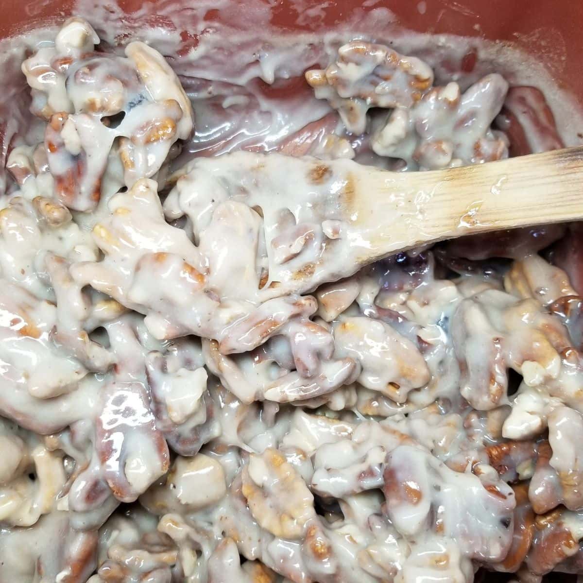 Pecans coated in the candy mixture. Stirring with a wooden spoon.