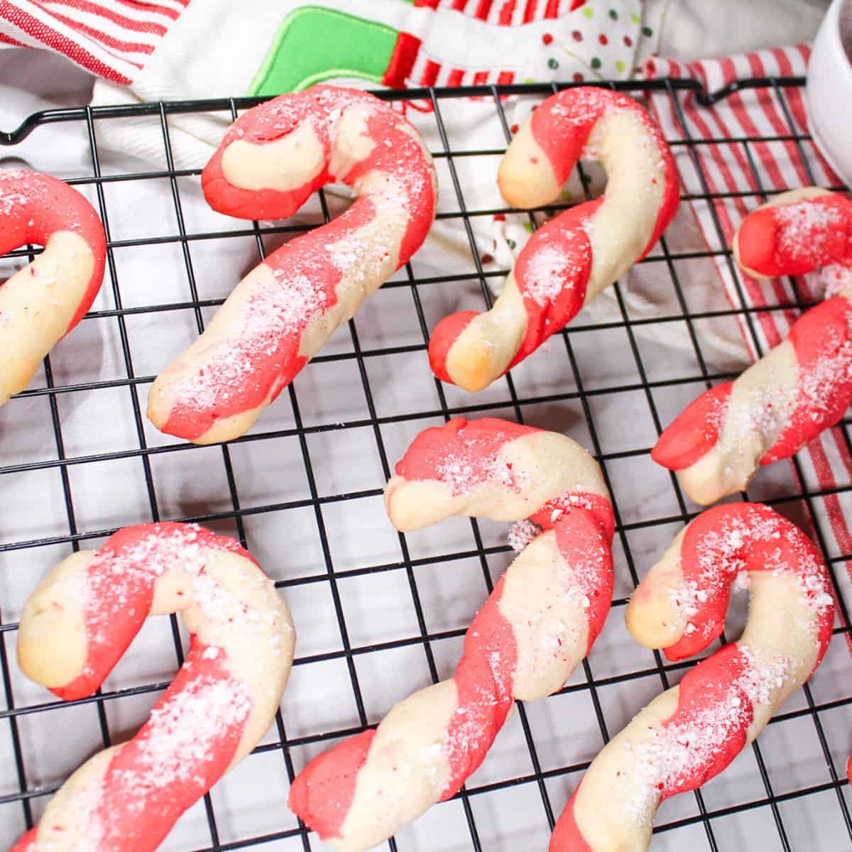 Candy cane cookies on a cooling rack with Christmas towels under the rack.