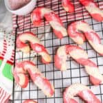 Candy cane cookies on a baking rack with Christmas towels next to the rack.