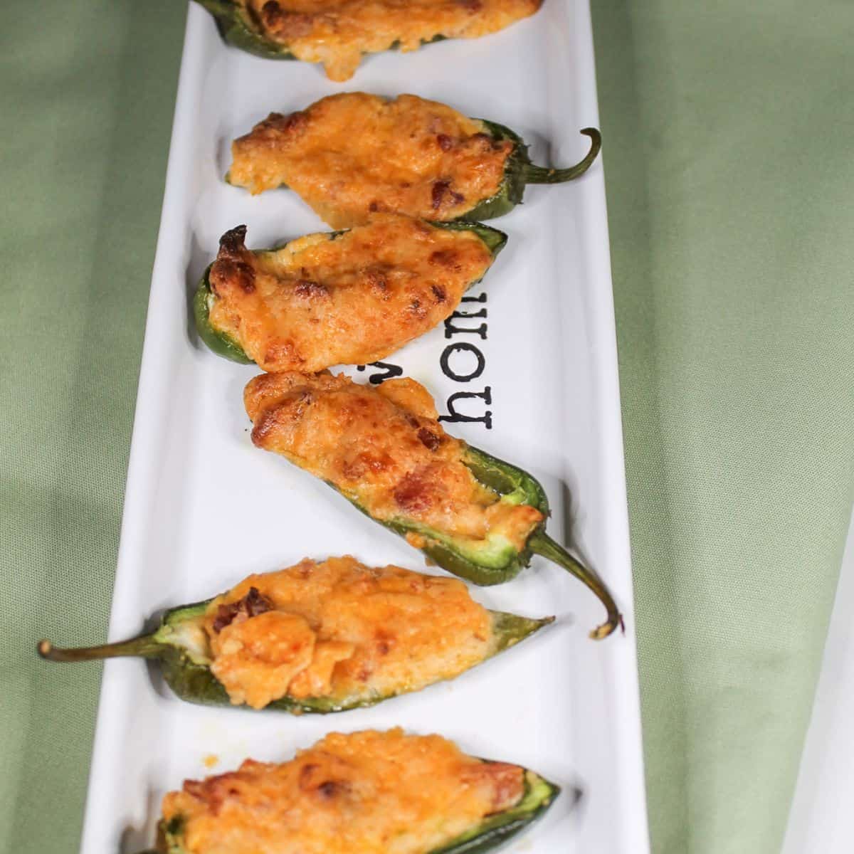 Baked jalapeno peppers on a white serving dish with a green kitchen towel.