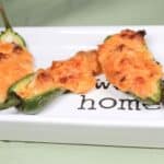 Baked cheese jalapeno peppers on a white plate.