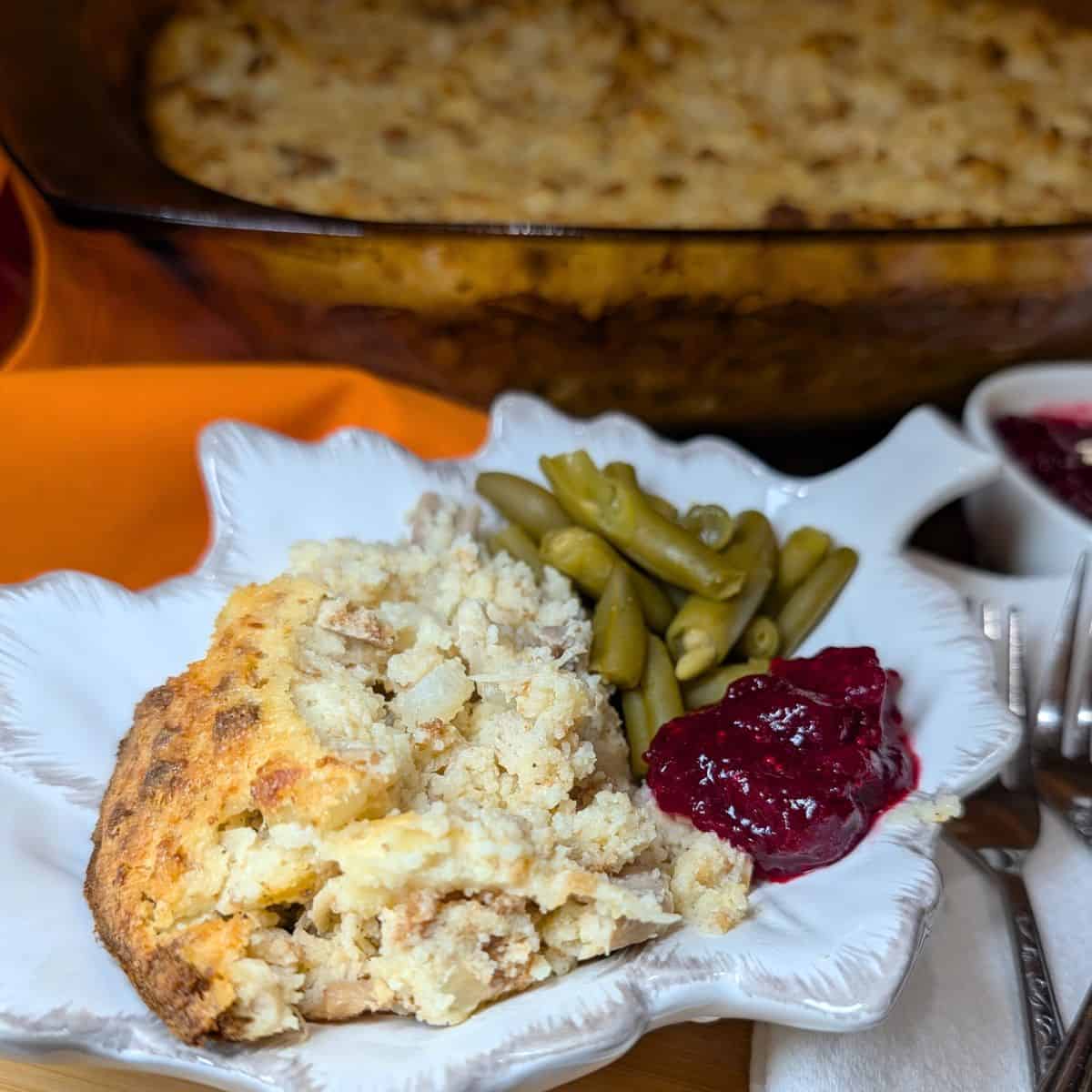 Southern chicken and dressing baked until golden brown in a casserole dish and served on a plate with cranberry sauce and green beans.