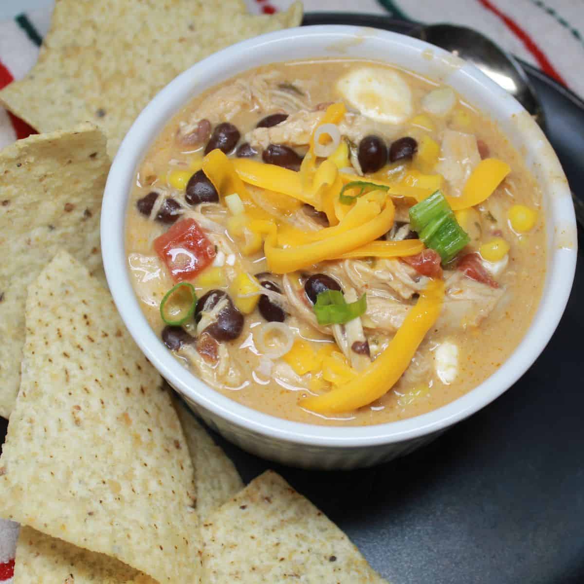 A bowl of chicken enchilada soup on a plate with chips.