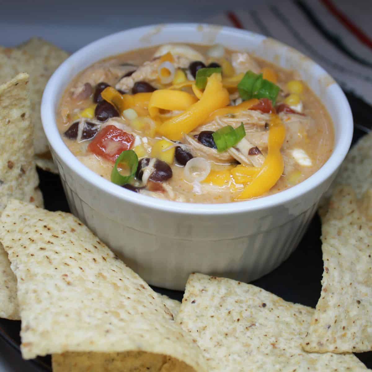 Enchilada soup in a white bowl with chips on the side.