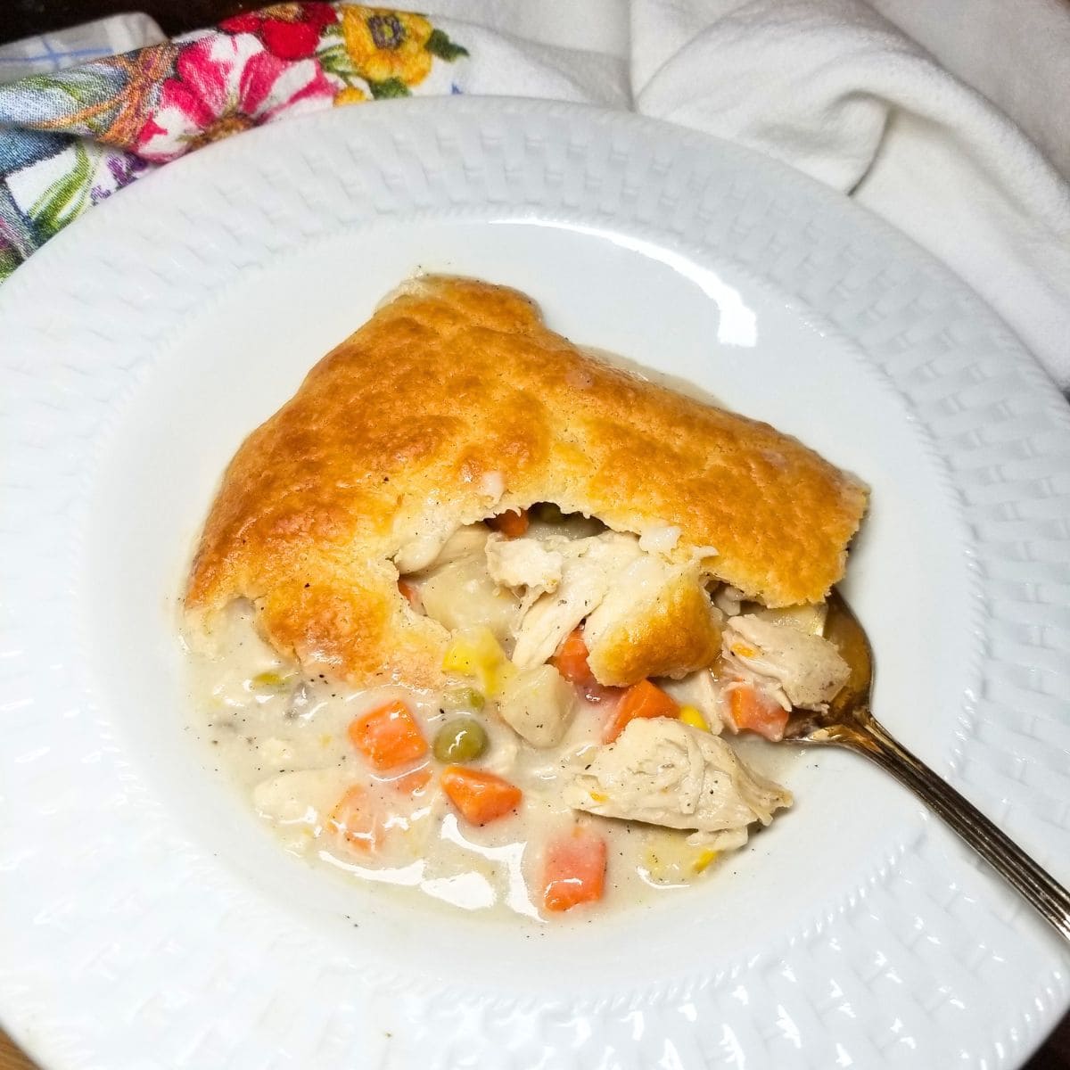Golden brown chicken pot pie fresh out of the oven in a white serving bowl.