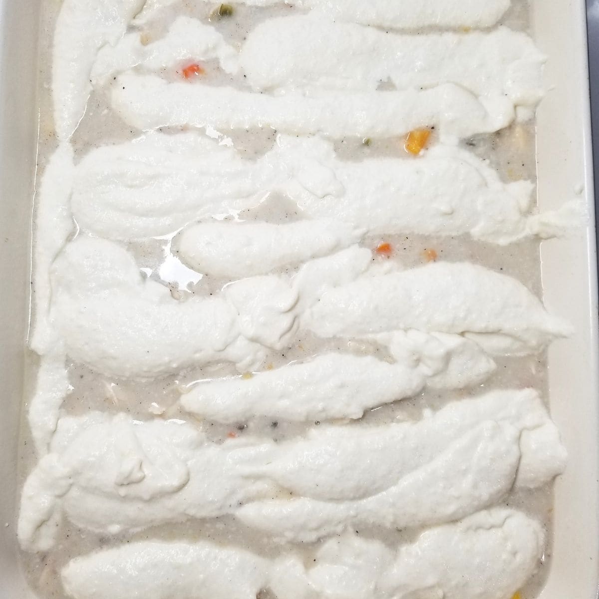 Spooning the topping over the chicken casserole in a baking dish.