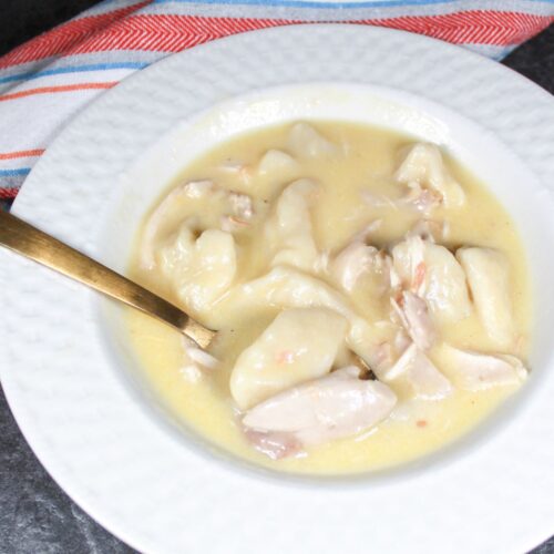 Chicken and Dumplings in a white bowl with a gold spoon. A stripped dish towel next to the bowl.