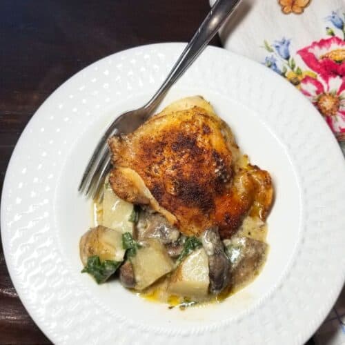 Baked chicken and potatoes in a white bowl with a fork read to serve.