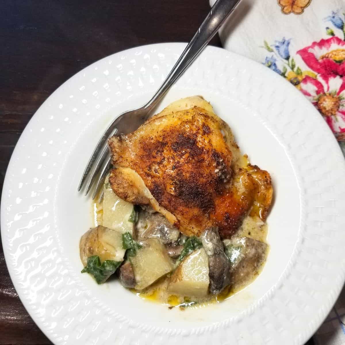 Chicken and potatoes with mushrooms, and spinach in a serving bowl with a fork.