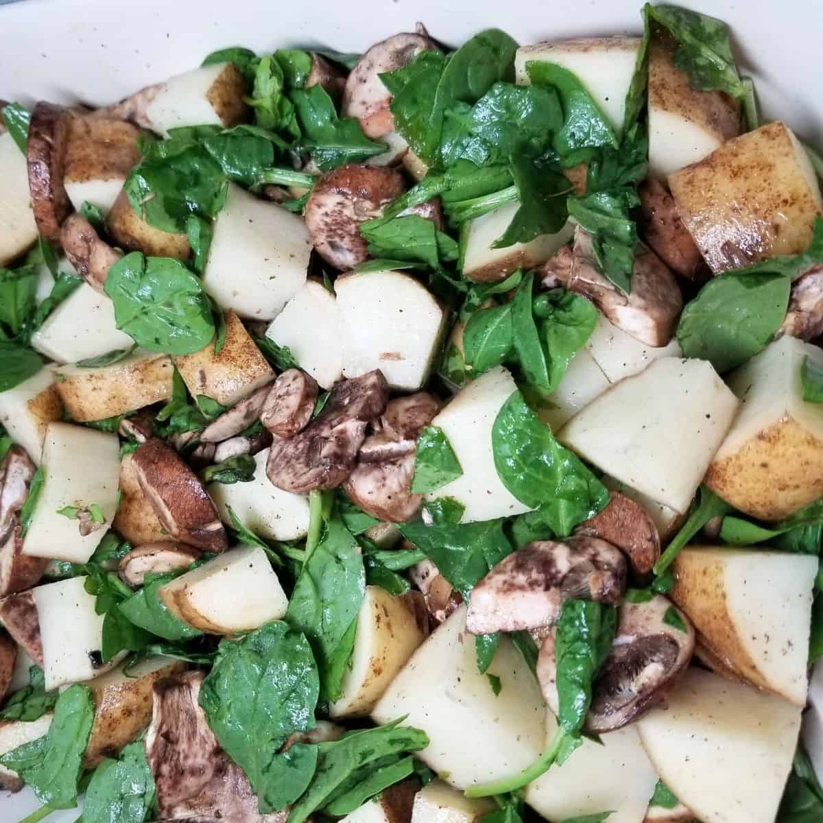 Diced potatoes, spinach, and mushrooms in a baking dish.
