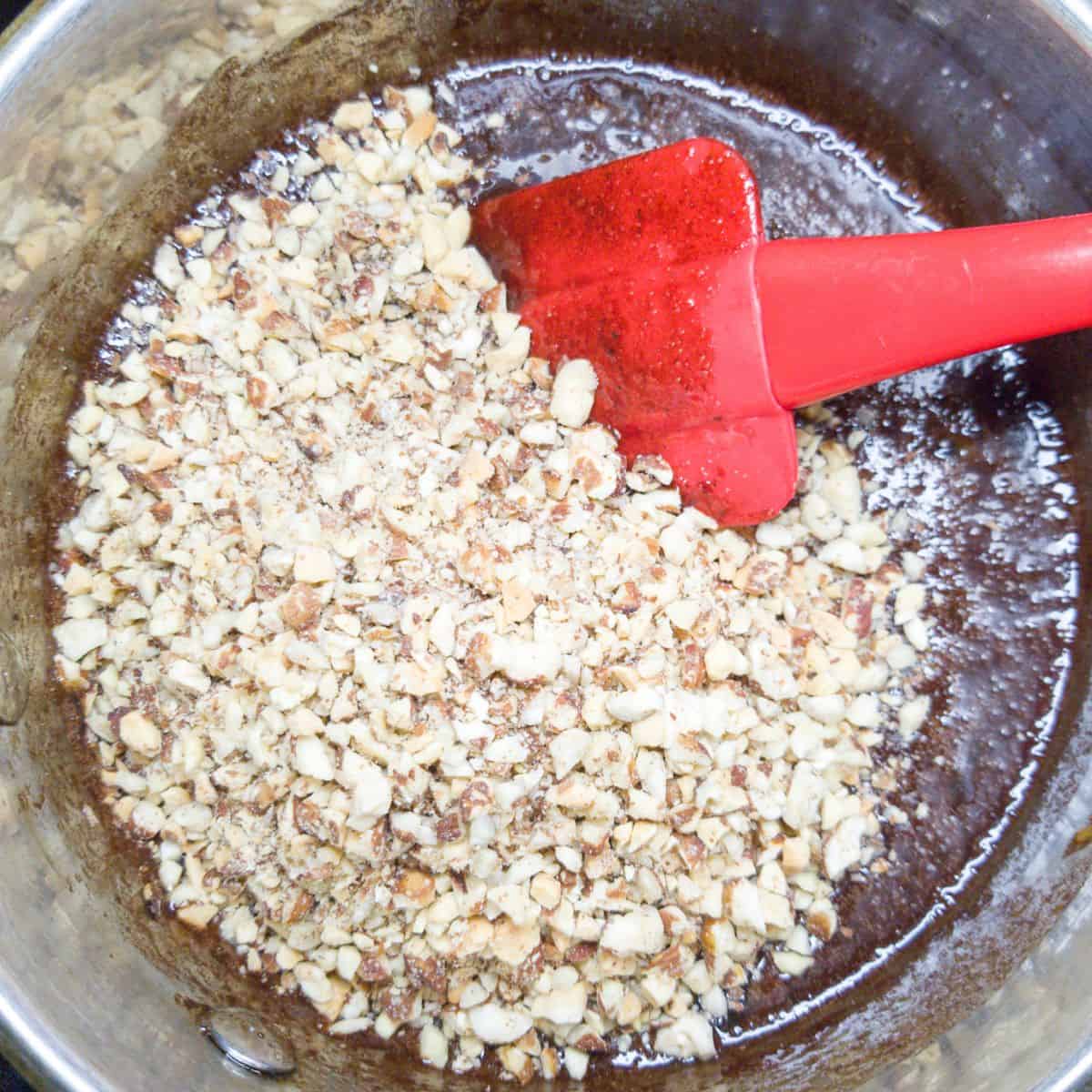 Chopped pecans in a pan with melted chocolate and a red spatula.