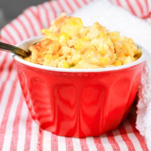 Corn casserole in a red bowl with a spoon.