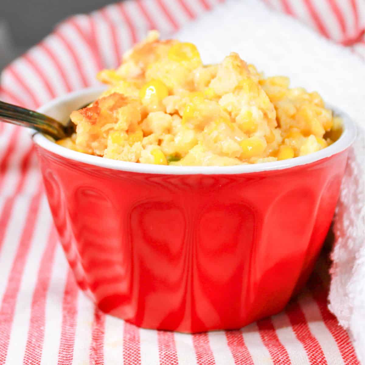 Corn casserole in a red bowl with a spoon.