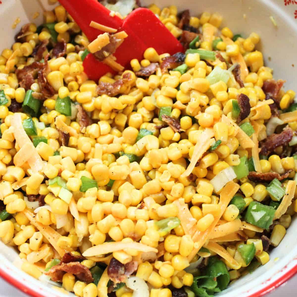 Corn salad in a red bowl with a red spoon.