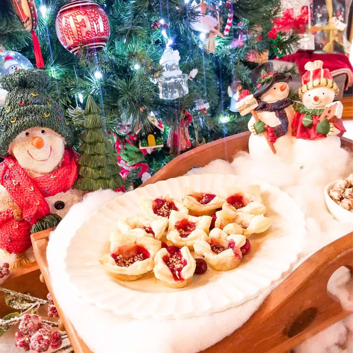The finished recipe with cranberry bites on a serving platter. A Christmas tree, several snowmen, and Christmas decor in the photo.