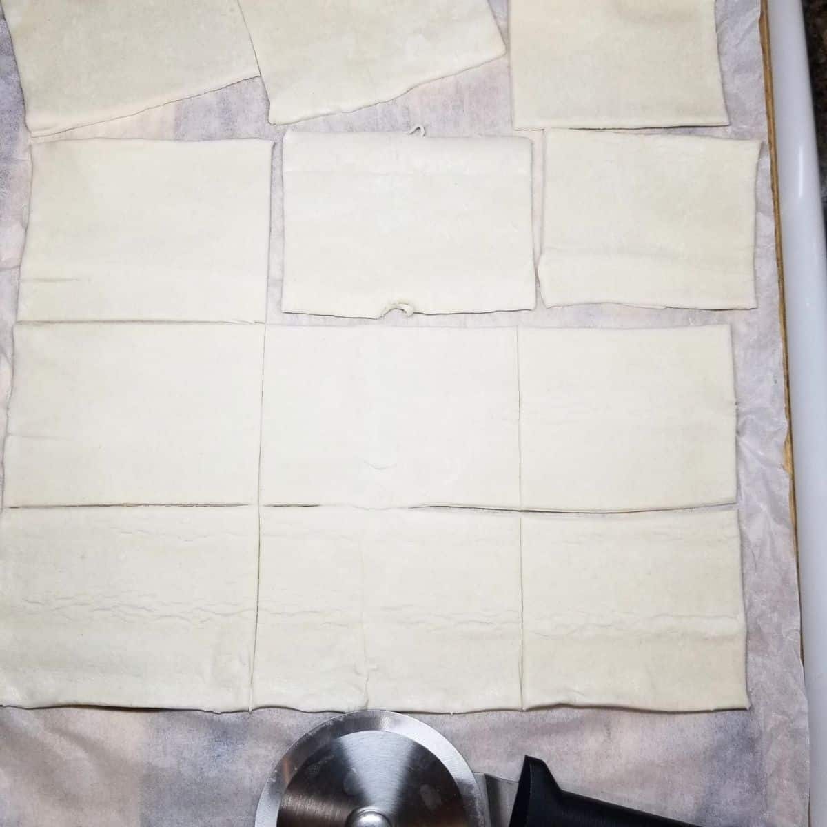 Puff pastry cut with a pizza cutter on a cutting board.
