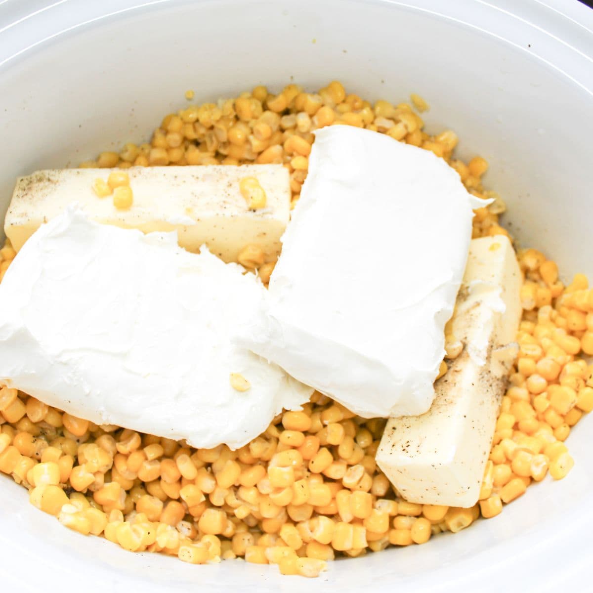 Whole corn in the bottom of a crock pot with cream cheese and butter on top.