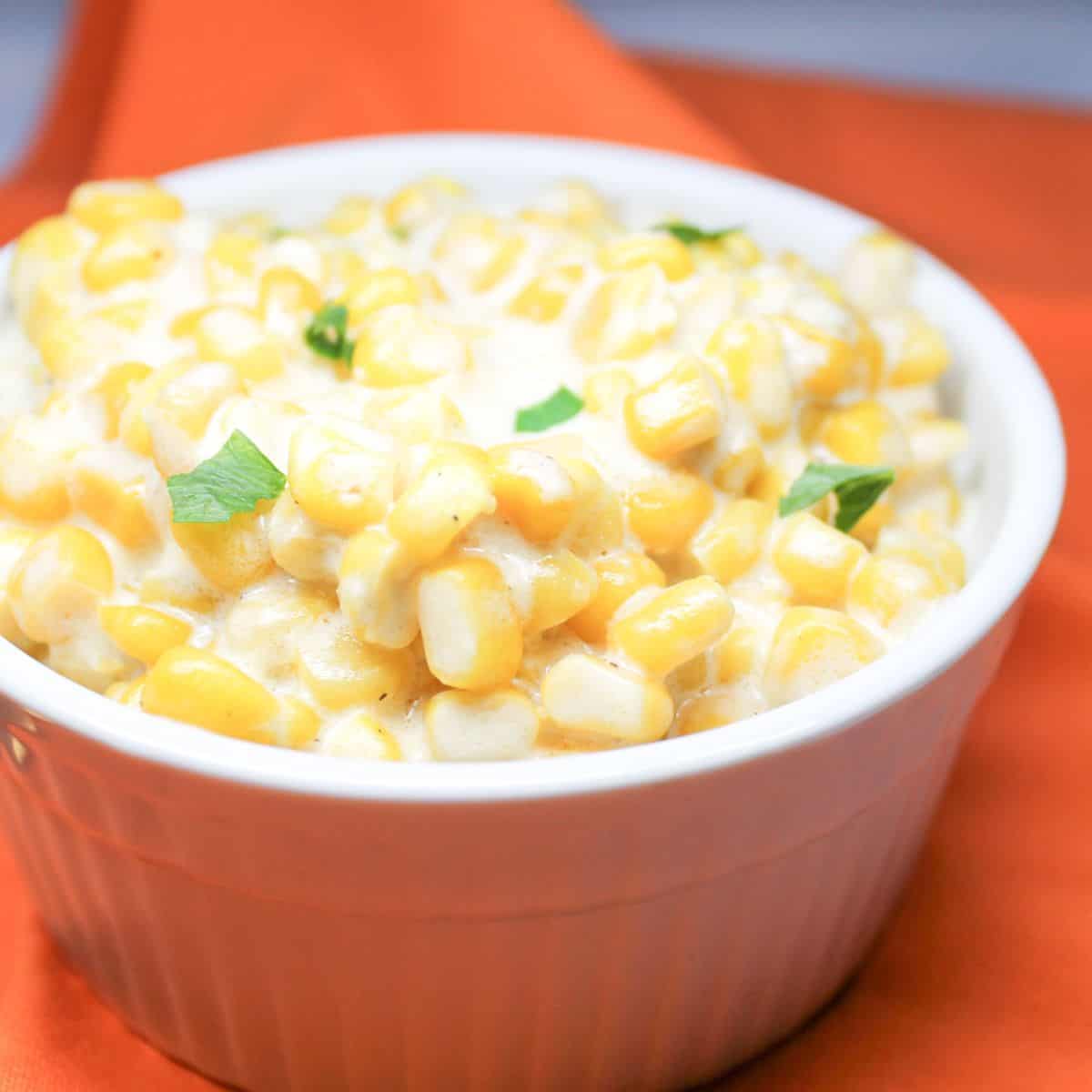 Creamed corn in a white bowl with an orange dish towel.