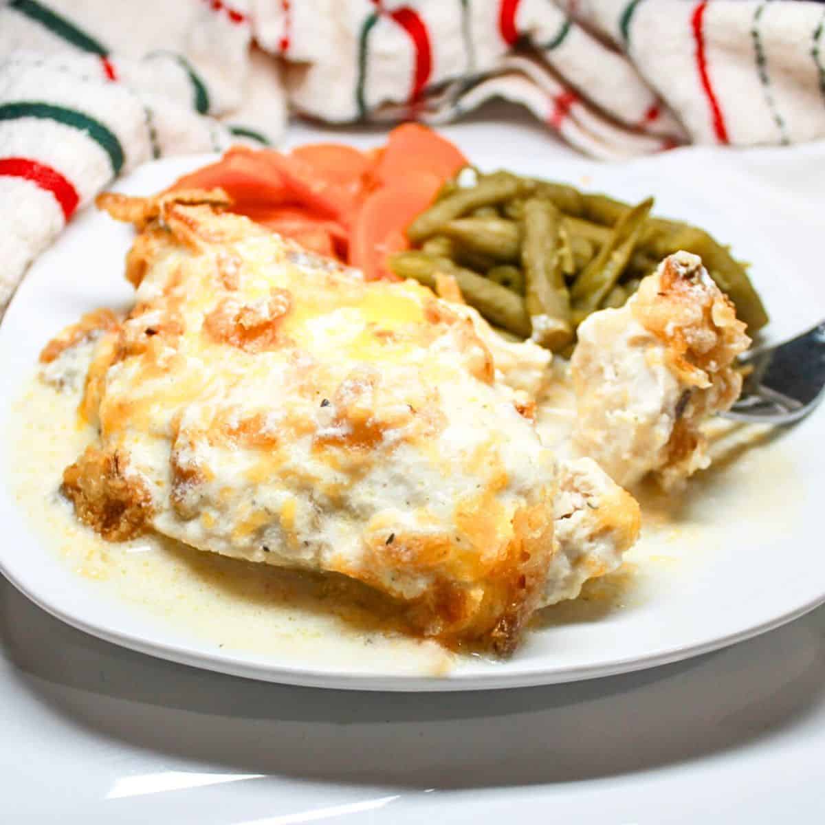 French onion chicken bake on a white plate with green beans and carrots.