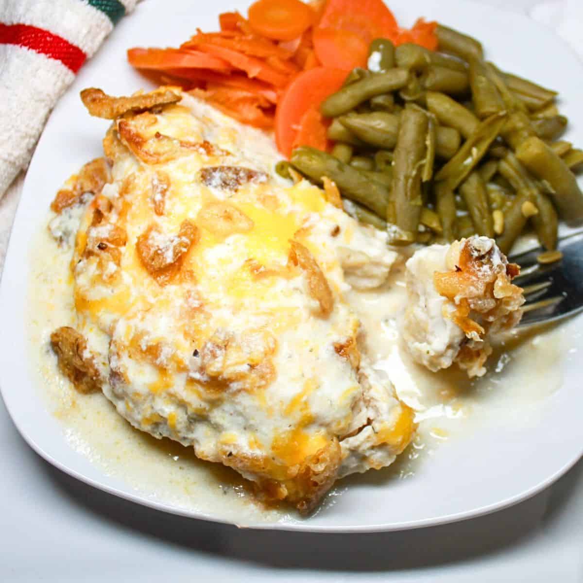 Chicken, green beans, and carrots on a white plate with a fork.