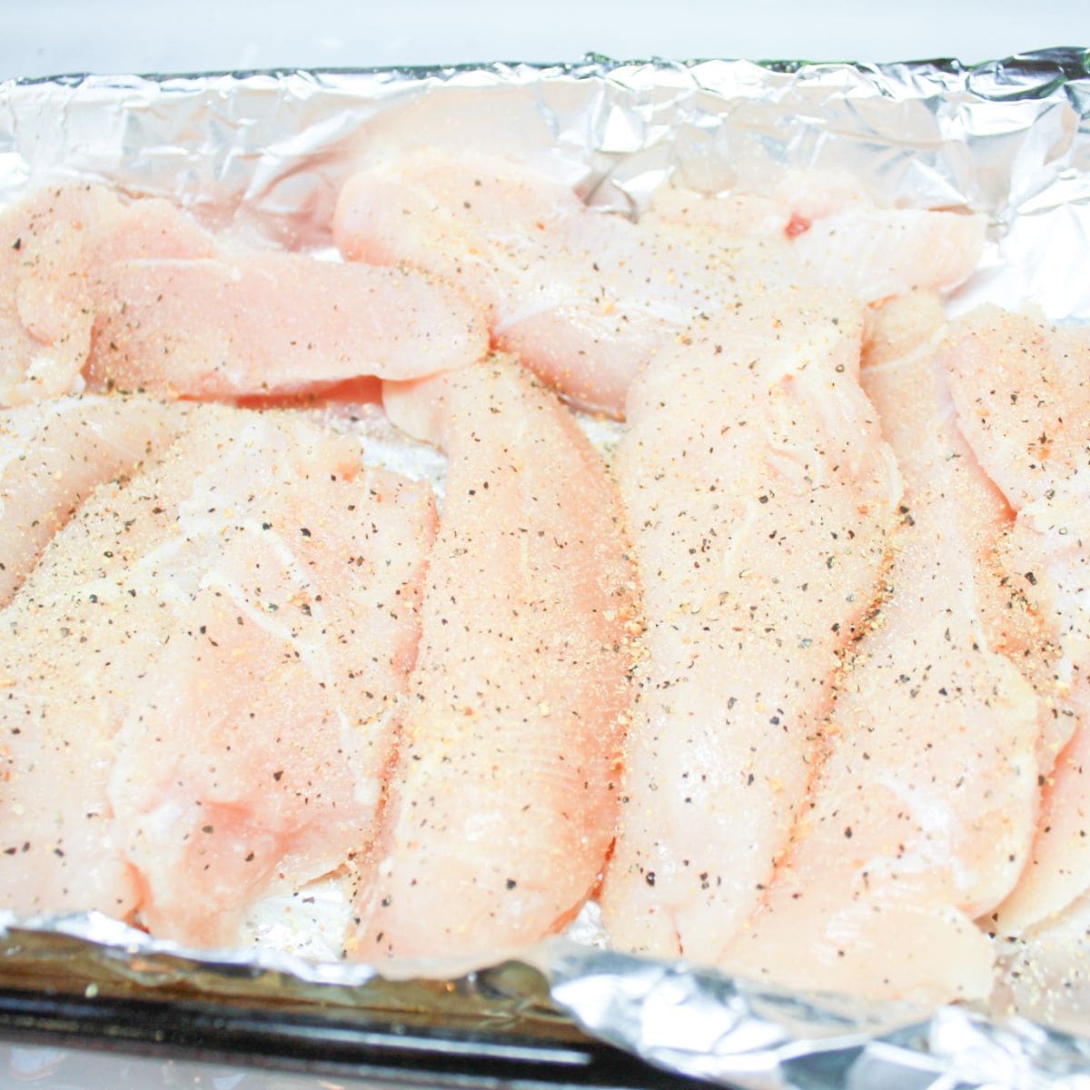 A baking dish lined with foil and topped with seasoned chicken tenders.