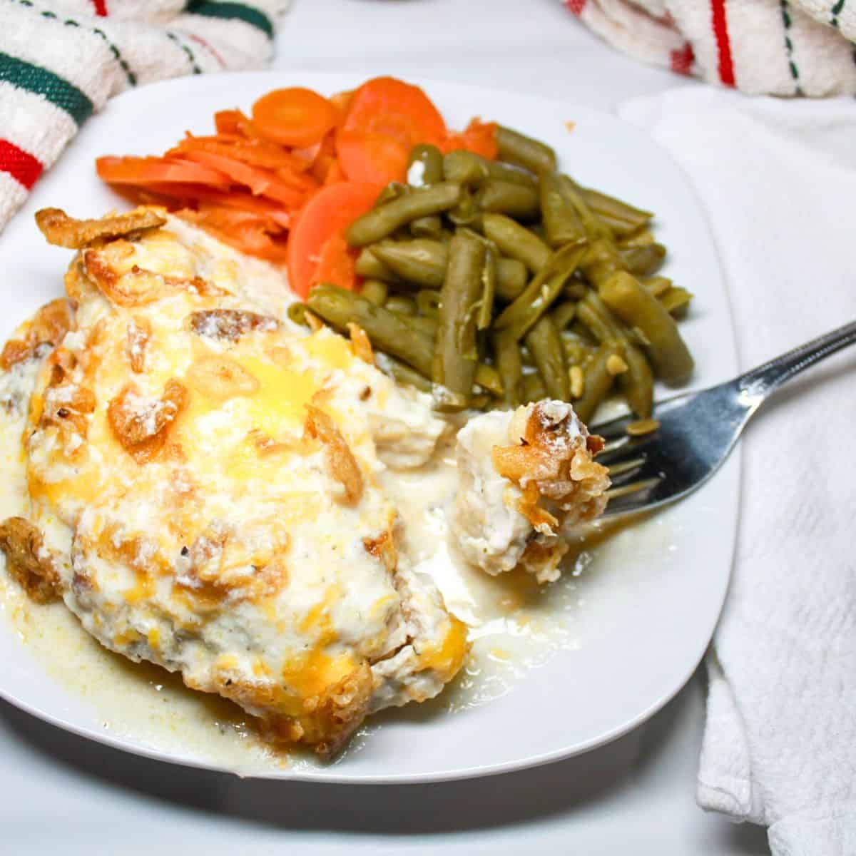Chicken, green beans, and carrots on a white plate with a fork.