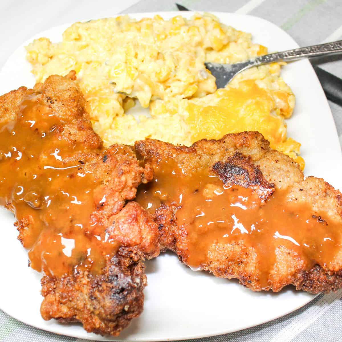 Fried cube steak and gravy with corn casserole on a white plate with a fork.