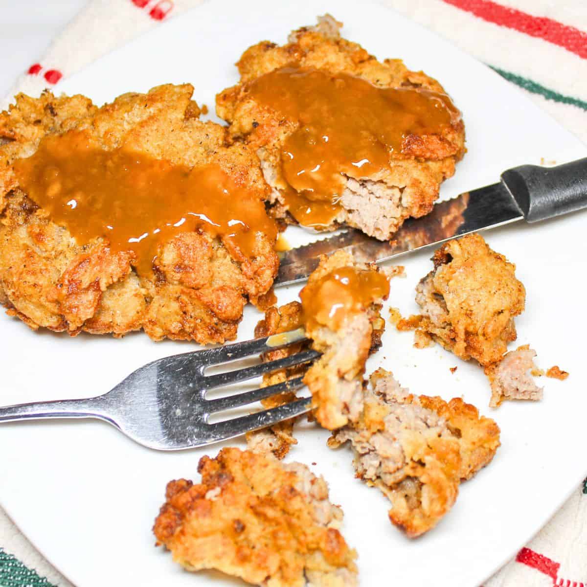 Fried cubed steak and gravy on a white plate with a fork and knife.